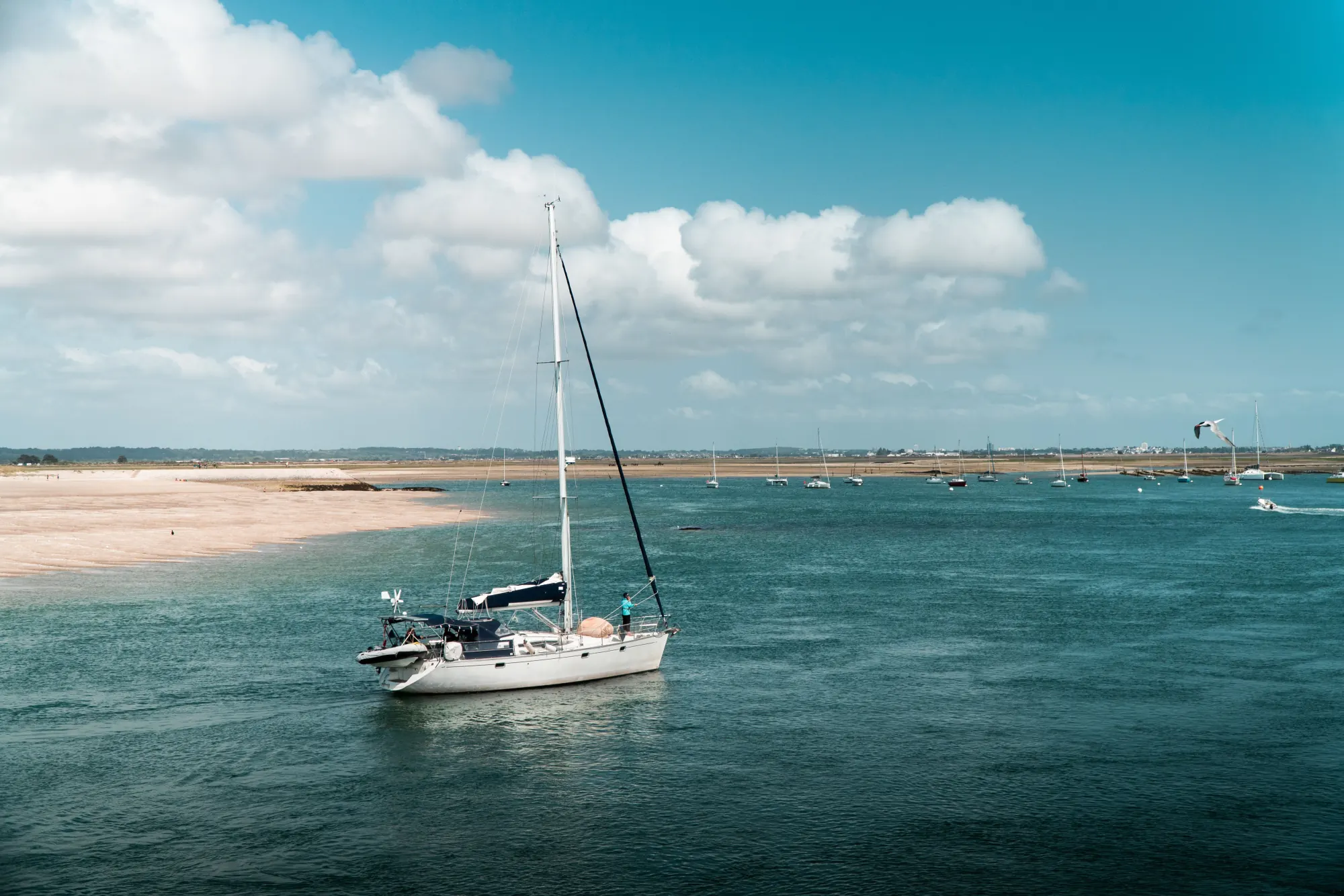White sailing yacht at anchor on calm blue water off a sandy shore