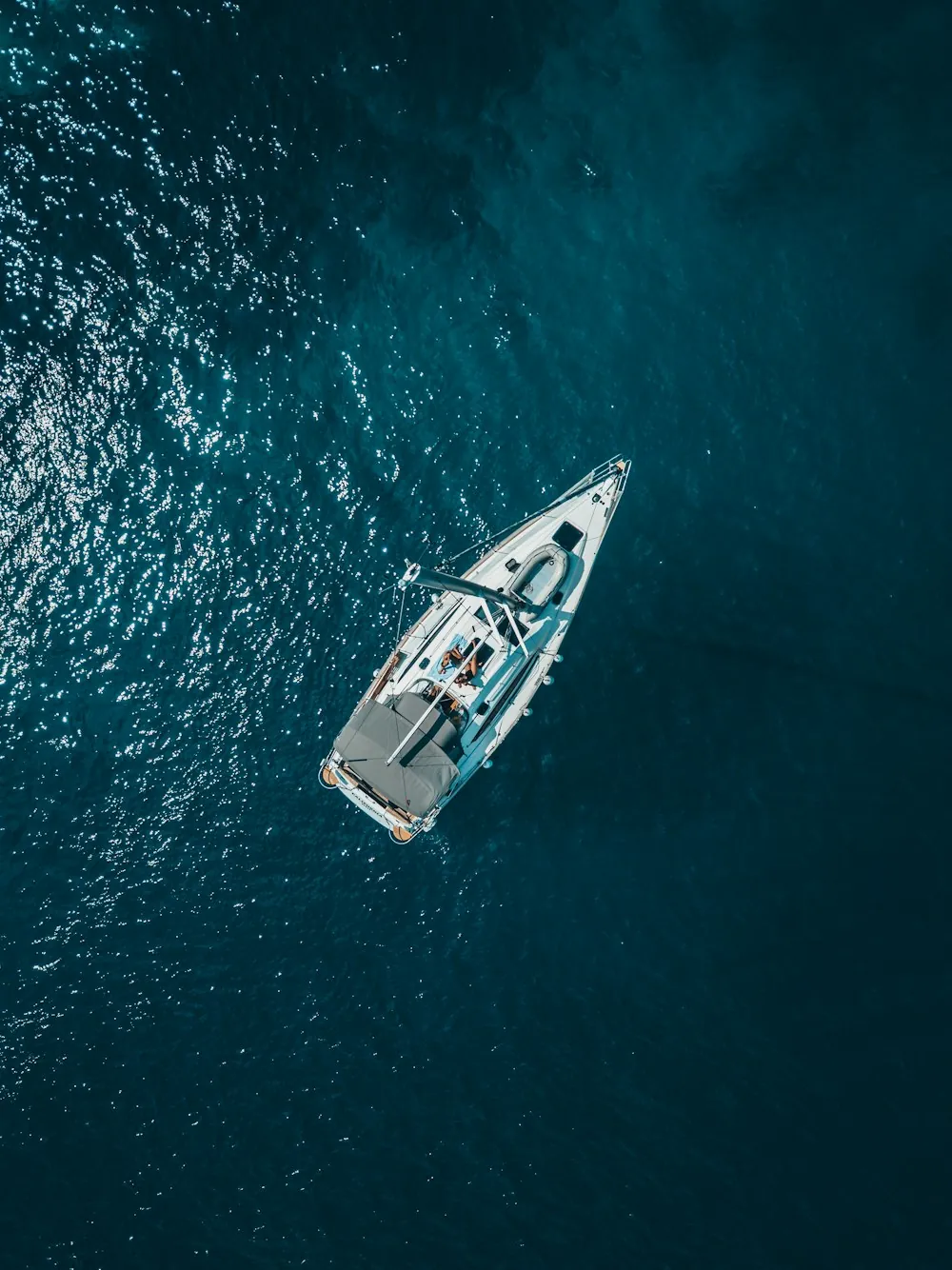 Aerial view of a white sailing boat on deep teal water