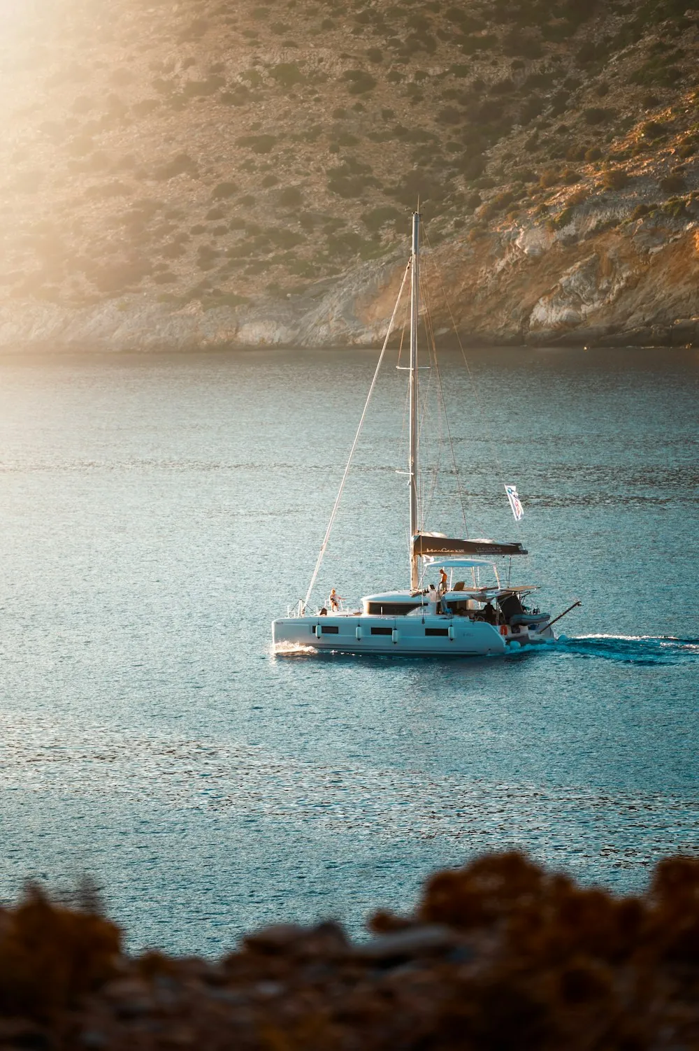 A sailing boat in warm evening light beside a rocky shore